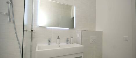 A modern bathroom with a glass shower enclosure, a white sink with a mirror above it, and a toilet.