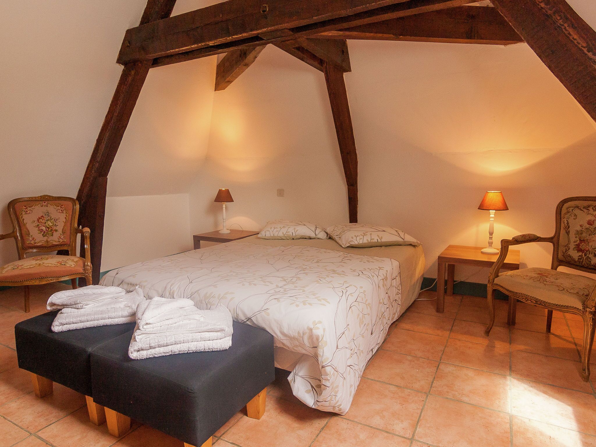 A bedroom with a large bed, two nightstands, two chairs, and a bench with towels.