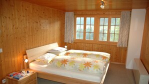Quarto com painéis de madeira, uma cama, uma mesa de cabeceira e uma janela com cortinas.