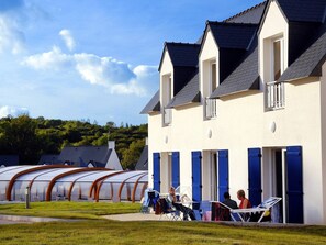 A building with a white facade and blue shutters, featuring a covered outdoor seating area with chairs and tables.