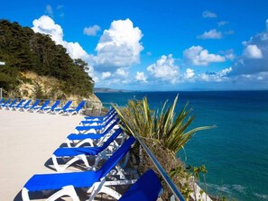Eine Strandlounge mit Reihen von Liegestühlen, freiem Blick auf das Meer und einer felsigen Küstenlinie.