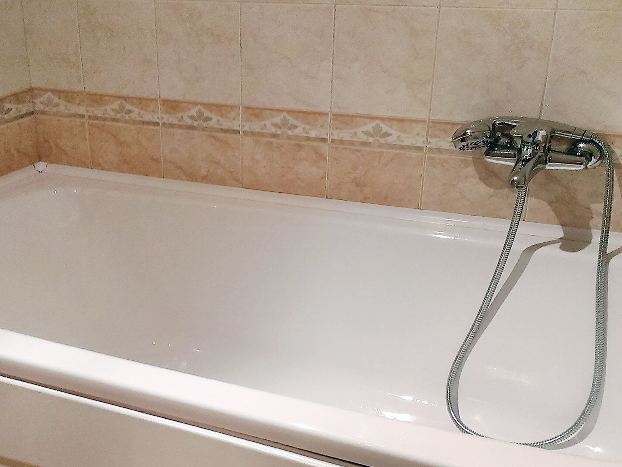 A white bathtub with a handheld showerhead, set against a tiled wall with a decorative border.