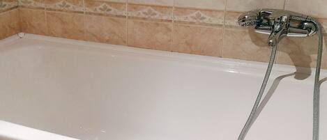 A white bathtub with a handheld showerhead, set against a tiled wall with a decorative border.