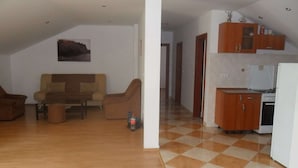 Een woonkamer met een bank en fauteuils, een keuken met houten kastjes en apparatuur, en een vloer met een geruit patroon.