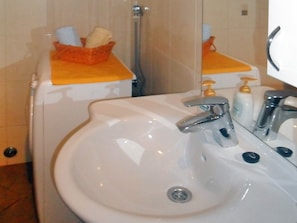 Een badkamer met een witte wastafel, twee kraanwerkers, een spiegel en een handdoekhouder met opgevouwen handdoeken.