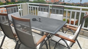 Een balkon met een tafel en stoelen, met uitzicht op een kustgebied met boten en gebouwen.