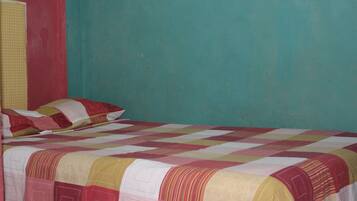Un letto singolo con copria letto in una stanza dalle pareti color acquamarina e una parete di colore rosso.