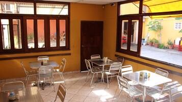 A restaurant interior with metal tables and chairs, a tiled floor, and large windows with wooden frames.