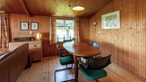 Une pièce aux murs lambrés, avec une table à manger en bois, des chaises à revêtement vert, un banc en bois, une radio et une carte accrochée au mur.