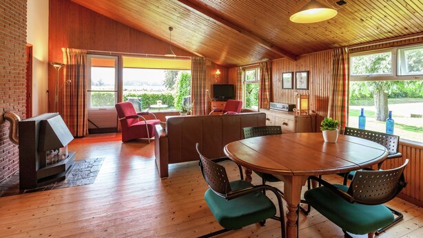 Un intérieur chaleureux avec un plafond en bois, un coin repas avec des chaises à revêtement vert, une cheminée et un téléviseur.