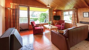 L’intérieur d’un chalet accueillant, avec des murs en bois, un canapé, deux fauteuils, une table basse, un téléviseur et une fenêtre avec des rideaux.