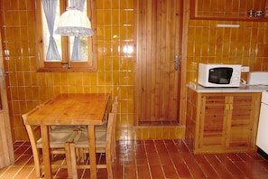 A wooden dining table with chairs, a microwave, and a small kitchen area with wooden cabinets and a tiled backsplash.