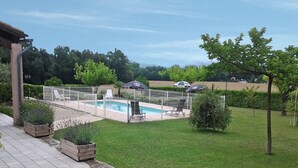Un jardín trasero con piscina, rodeado por una cerca y un césped con algunos árboles.