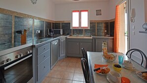 Una cocina moderna con horno empotrado, microondas y lavaplatos. Hay una mesa de comedor con sillas y una ventana con cortinas.