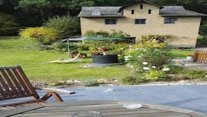 A patio with a wooden table and chairs, a hot tub, and a house in the background.