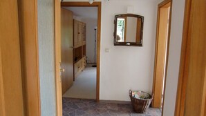 A hallway with a stone floor, wooden cabinets, a mirror, and a wicker basket.