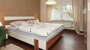 A bedroom with a bed, a window with curtains, a radiator, and a hanging light fixture.