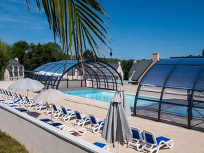 A pool area with lounge chairs and umbrellas, surrounded by glass enclosures.