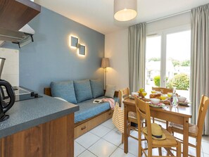 A modern kitchenette with a built-in oven, a dining area with a table set for breakfast, and a sofa with a view of the outdoors.