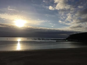 Ein Strandbild mit untergehender Sonne über dem Wasser, Booten und einer fernen Küste.