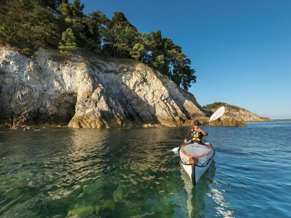 A kayaker on a calm body of water with clear visibility, surrounded by rocky cliffs and dense trees.