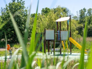 Ein Spielplatz mit Rutsche und Klettergerüsten, umgeben von viel Grün.
