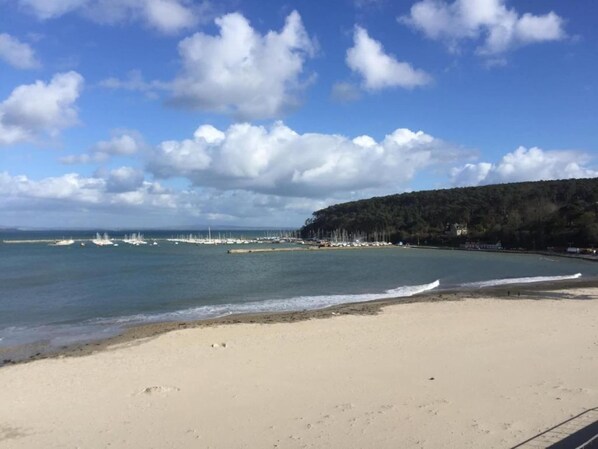 Ein Strand mit sandigem Ufer, ruhigem Wasser und einer bewaldeten Hügelkette im Hintergrund.