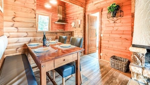 Interior de una cabaña de madera con comedor, chimenea y pared de piedra.