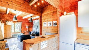 Interior de una cabaña de madera con cocina, comedor y vistas al exterior.