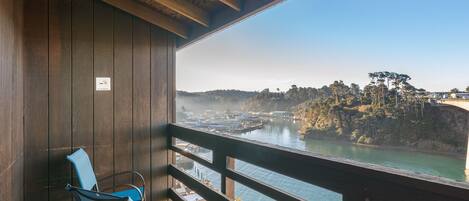 A wooden balcony with a view of a river and distant hills.