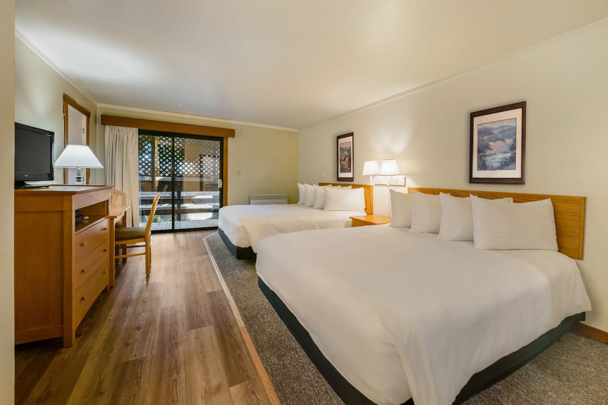 Habitación de hotel con dos camas, un escritorio con silla, televisión y balcón con vistas.