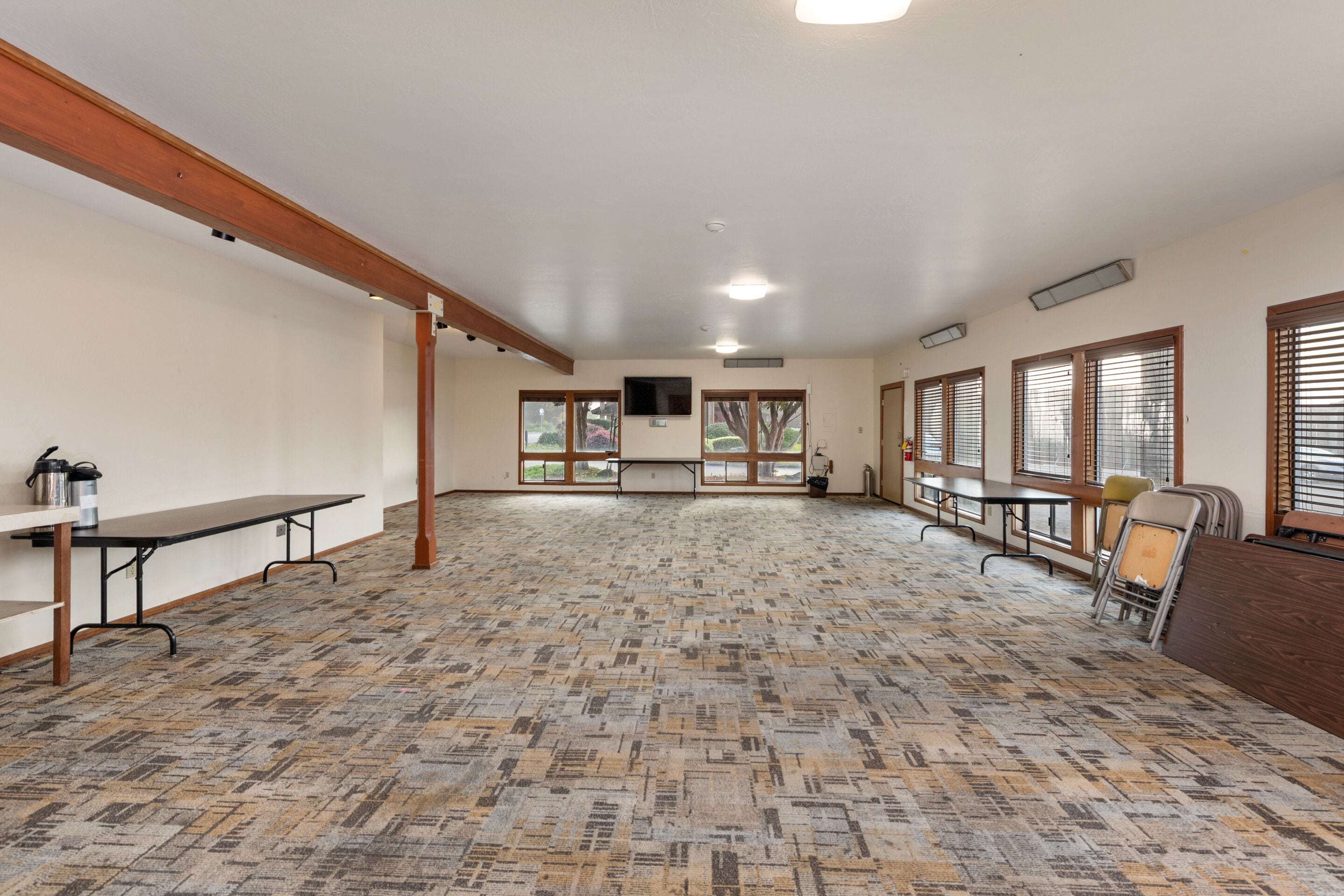 Una habitación amplia con alfombra estampada, vigas de madera y ventanas grandes.