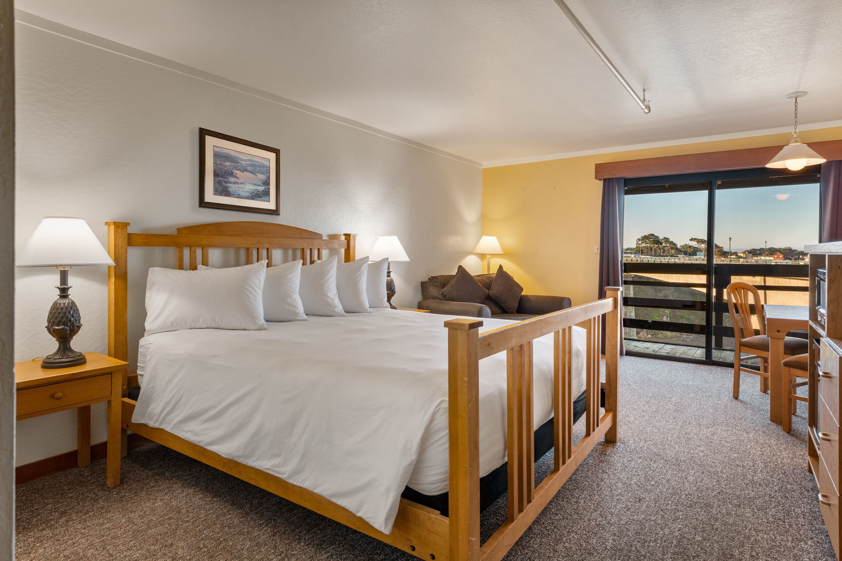 A bedroom with a wooden bed, two bedside tables with lamps, a sofa, and a balcony with a view.