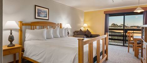 A bedroom with a wooden bed, two bedside tables with lamps, a sofa, and a balcony with a view.