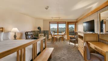 A hotel room with a bed, desk, chair, and a TV. There is a window with a view of trees.