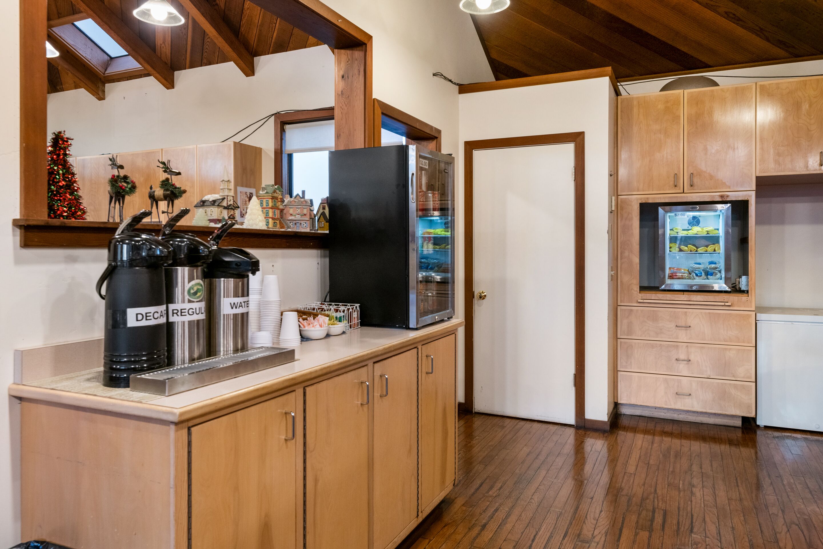 A kitchen with wooden cabinets, a refrigerator, and a coffee station with decaf, regular, and water options.