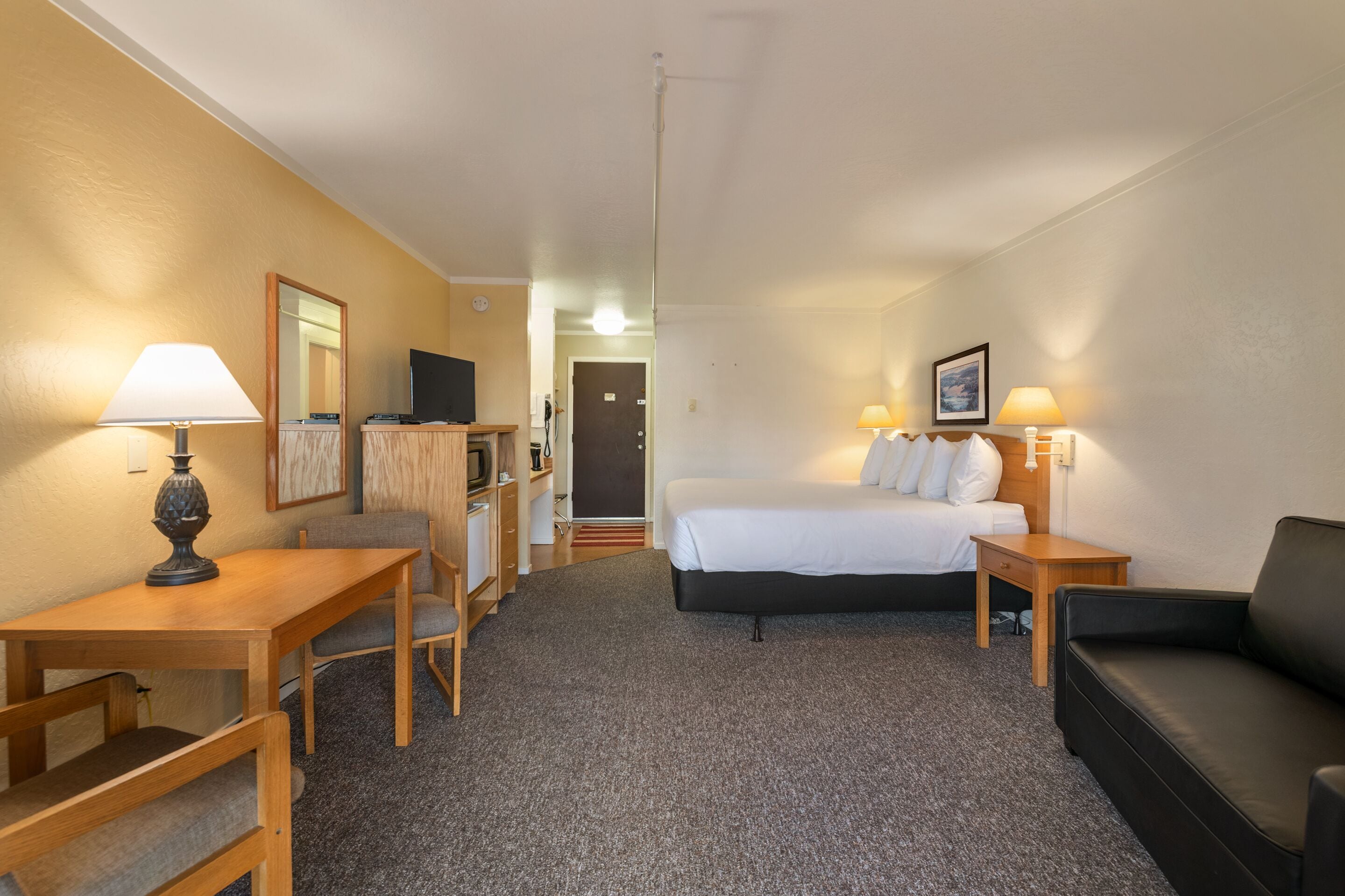 A hotel room with a bed, a desk, a chair, a couch, and a TV.