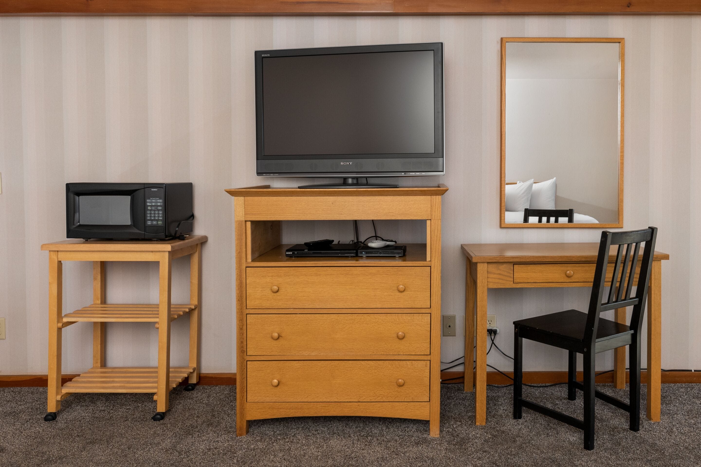 Une chambre d’hôtel équipée d’un bureau en bois, d’une télévision, d’un four à micro-ondes, d’une chaise et d’un miroir.