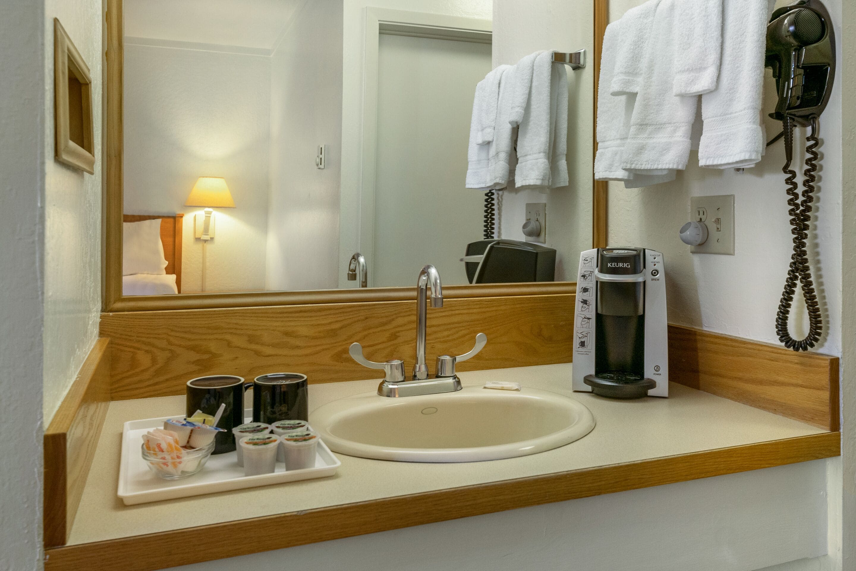 Un baño de hotel con lavamanos, espejo, toallero, secador de pelo y cafetera.
