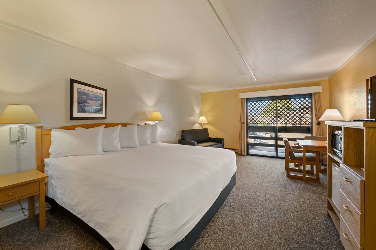 Habitación de hotel con una cama grande, un escritorio, una silla, un televisor y un balcón con puerta celosíaca.