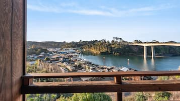 A view from a wooden balcony overlooking a riverside town with a bridge, buildings, and greenery.