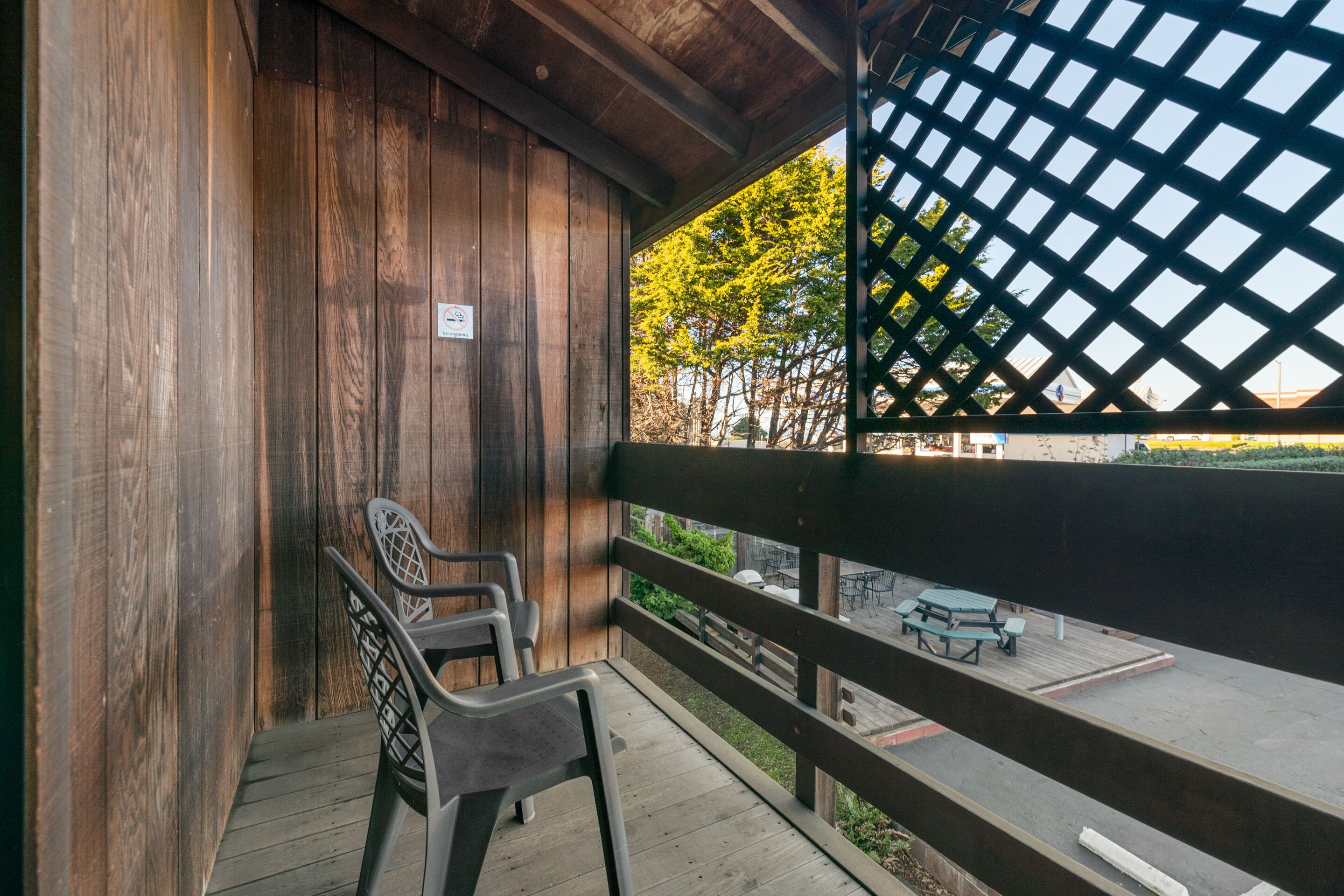 A balcony with wooden walls and a lattice railing. There are two chairs and a table on the balcony.