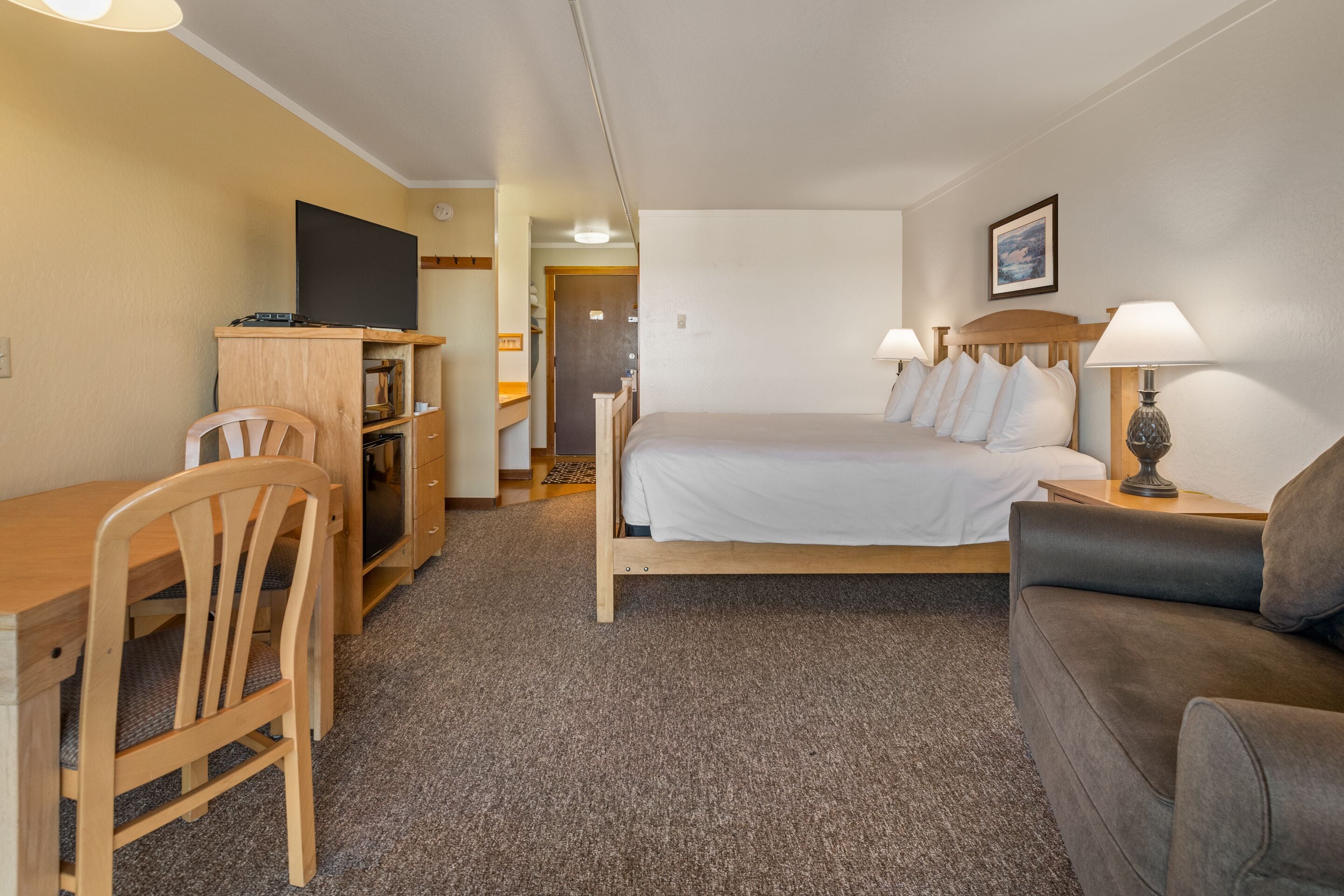 A hotel room with a bed, a desk, a chair, a sofa, a TV, and a lamp.