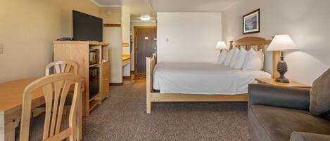 A hotel room with a bed, a desk, a chair, a sofa, a TV, and a lamp.