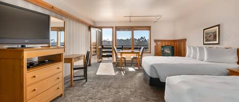 A hotel room with a large flat-screen TV, a desk with a chair, two beds, and a view of the outdoors.