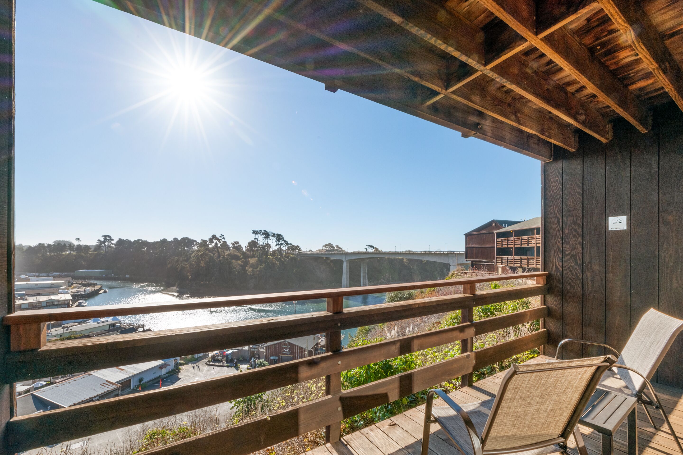 Una terraza de madera con vista a una zona costera, que incluye un puente y edificios.