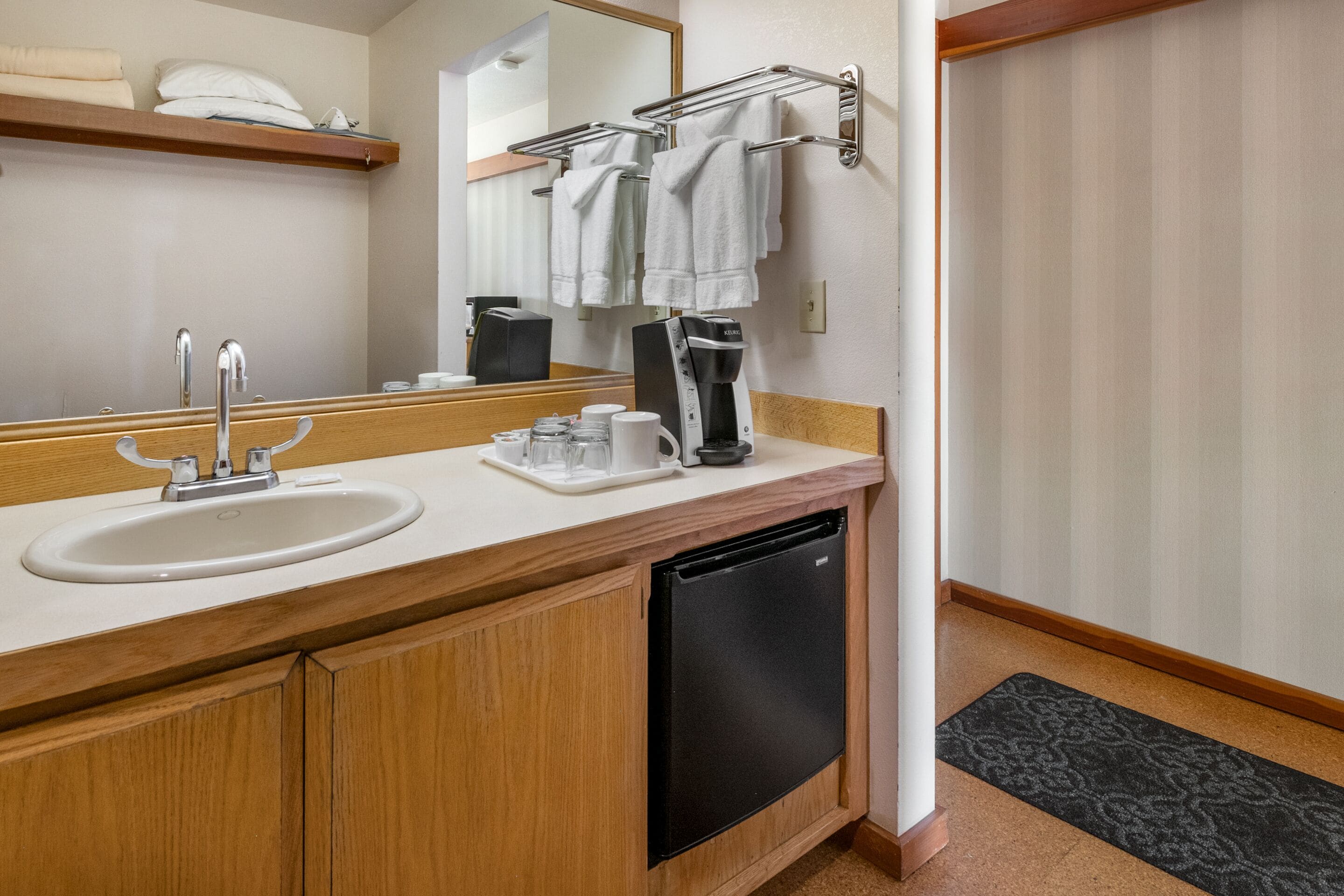 Een moderne badkamer met een wastafel, spiegel, handdoekhouder en een koffiezetapparaat.