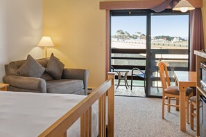 A hotel room with a bed, a sofa, a table, and a chair. There is a view of the beach through the glass door. - Harbor Lite Lodge (Fort Bragg)