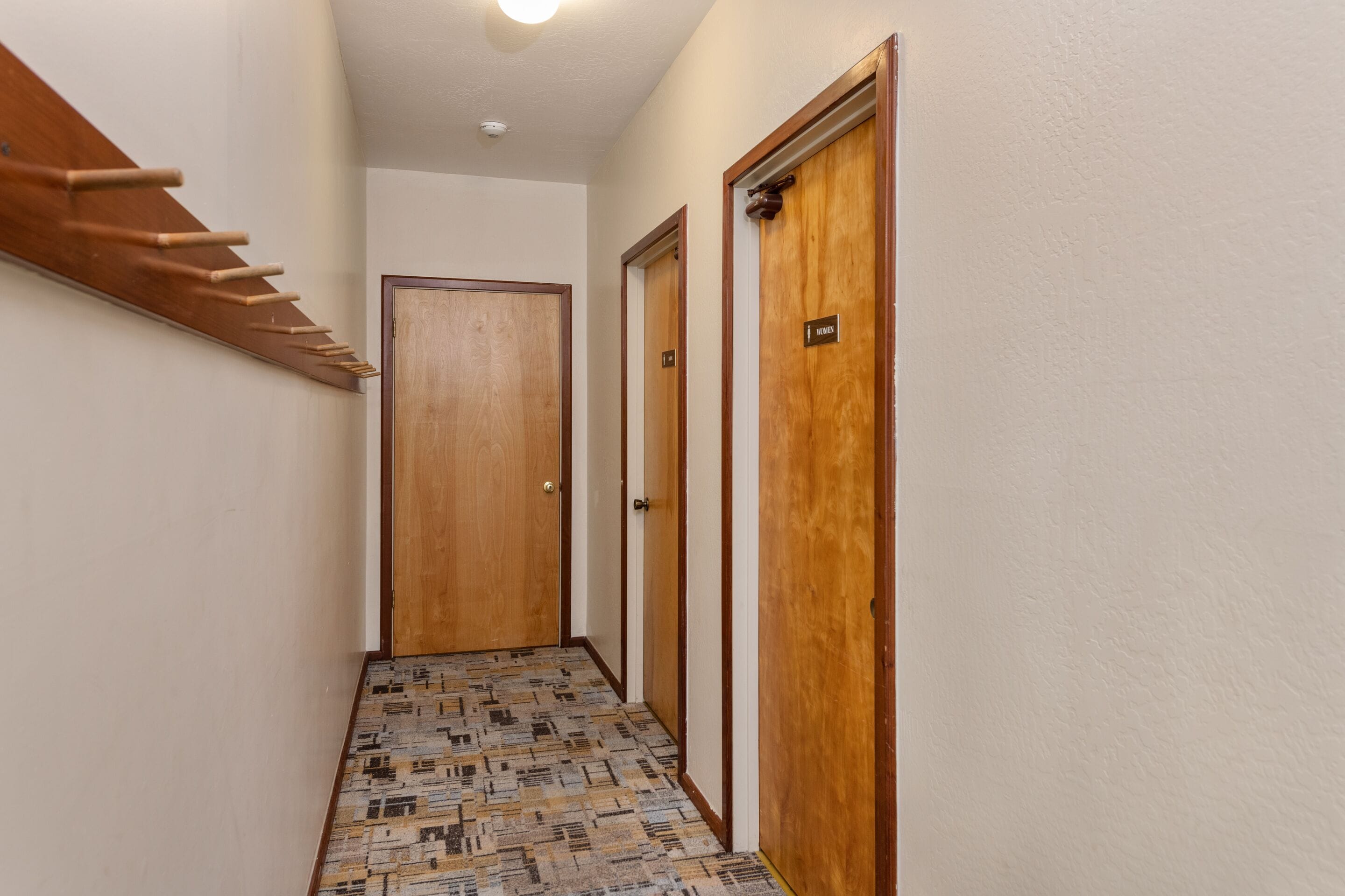 A narrow hallway with patterned flooring, wooden doors, and a coat rack.