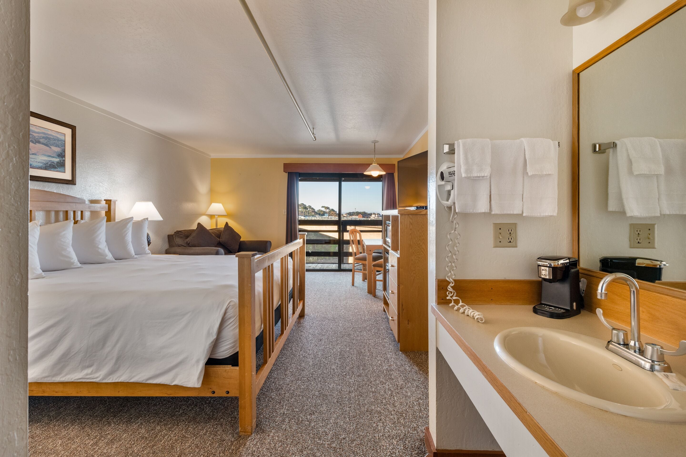 A hotel room with a bed, a desk, a chair, a sink, and a view of the outside.